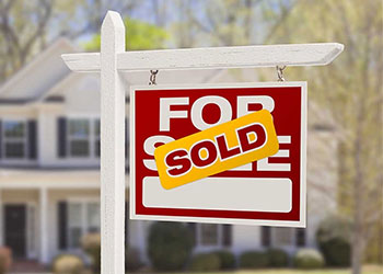Sold sticker over a for sale sign in front of a home